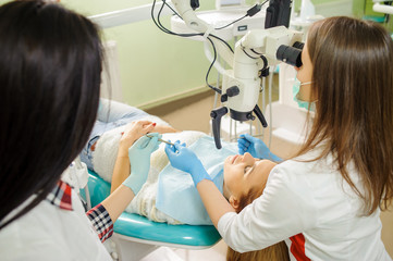 Female dentist and assistant in a dental hospital, wearing masks and gloves. Beautiful woman dentist holding dental tools getting ready for teeth treatment with microscope.