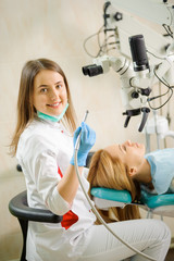 Portrait of beautiful female dentist holding stomatology tool, using microscope, smiling and looking at the camera at the dentist office. Dental care and treatment. Successful treatment