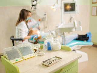 Dental tools on foreground and female dentist with assistant doing first check-up on the background. Medical equipment. Specialized equipment to treat all types of dental diseases in the clinic.