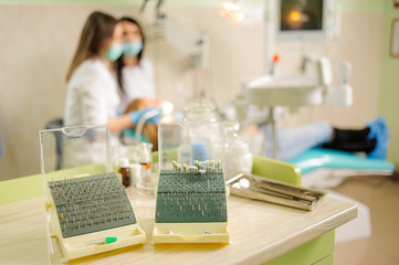 Dentistry drills, polishers and polishing brushes eraser on foreground and dentist with assistant checking patient teeth on the background. Specialized equipment for treating teeth in the hospital - obrazy, fototapety, plakaty