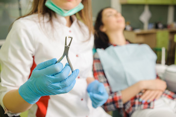Female dentist holding tool for removing brackets on foreground and female patient on the background. Orthodontic Treatment. Stomatology equipment at the dental clinic