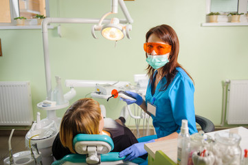Female dentist doctor is holding dentist photopolymer lamp getting ready to treat patient in clinic. Dentist is wearing gloves and glasses and looking to the camera. Medical equipment.