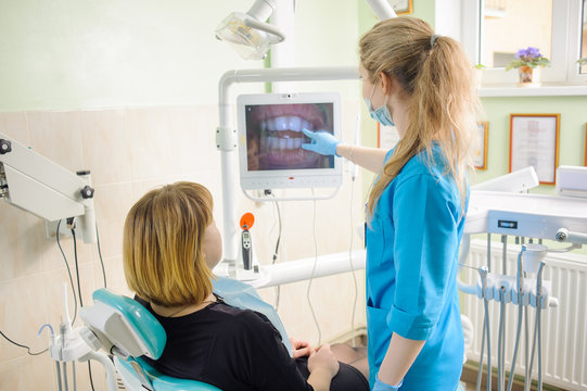 Young female dentist showing photograph of teeth on computer to her patient in modern dental office. Dental care and treatment. Successful treatment