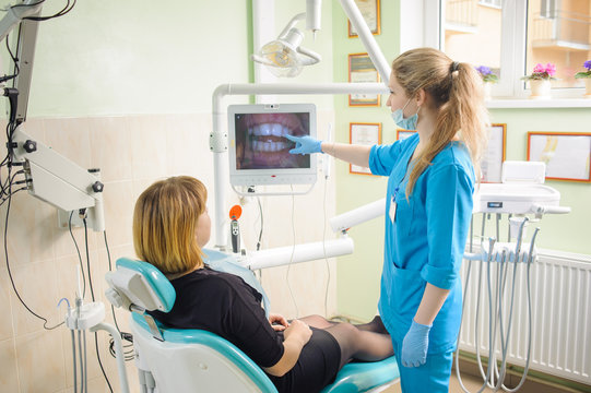 Young woman dentist showing photograph of teeth on computer to her patient in modern stomatology office. Teeth care and tooth health. Successful treatment