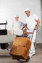 Worker Pushing Bread Loaves On Pushcart While Coworker Smiling
