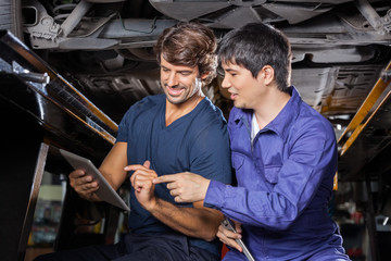 Mechanics Using Tablet Computer Under Lifted Car