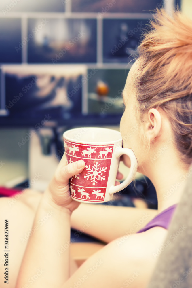 Wall mural woman with a cup of coffee sitting in front of computer screen, looking at the pictures on the web