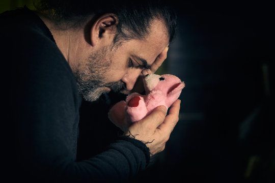 Sad man holding pink teddy bear, concept of loss and mournig