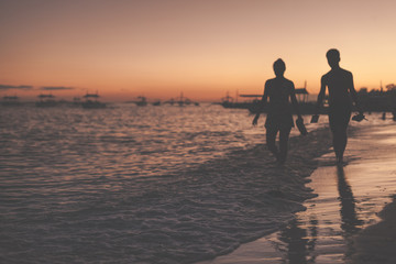 Traditional philippine boats floating in the sea and silhouettes of a woman and man walking along the sea shore during sunset. Panglao Island, Philippines.