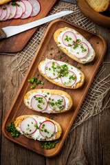 Fototapeta na wymiar Toasts with radish, chives and cottage cheese on a wooden table.