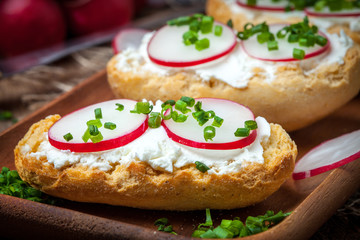 Toasts with radish, chives and cottage cheese on a wooden table.