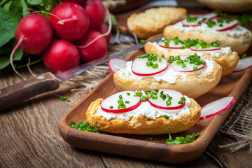 Toasts with radish, chives and cottage cheese on a wooden table.
