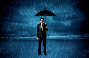 Business man standing in rain with an umbrella