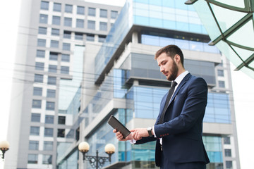 Fototapeta premium Businessman holding tablet on background of buildings with glass facades