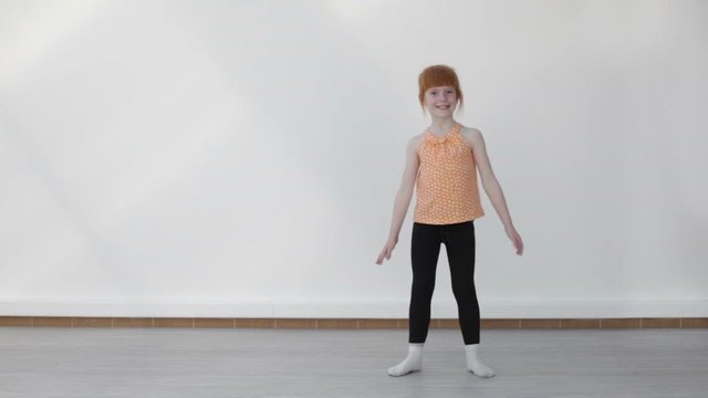 Little red-haired girl performing the wheel exercise ( dynamic handstand), white background, long shot