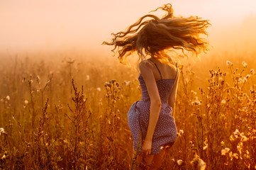 Dancing beautiful girl in fog, field, sun backlight, sunrise, orange colors