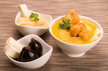 Traditional fanesca serving sitting on grey textile surface with accessories next to it such as molo mashed potatoes and fig dessert