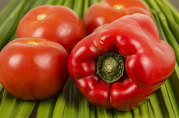 Red big pepper with three brights tomatoes on a green vegetables surface