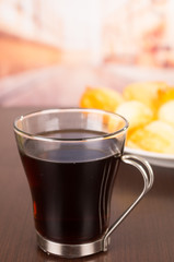 Little cup with coffee and metal handle on table, blurry plate of food in background