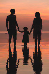 Silhouette of two adults and a child at the sea