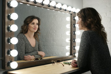 Молодая женщина смотрится в зеркало с лампами