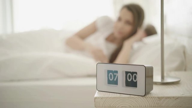 4k footage, focus on alarm clock, young woman streching and waking up
