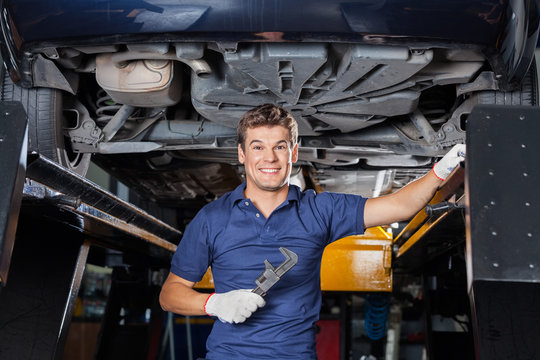 Mechanic Holding Wrench Underneath Lifted Car
