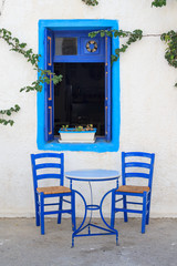 Table and chairs in front of a greek house with window - 109360325