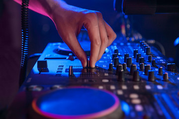 dj hand on mixing controller in blue light. closeup