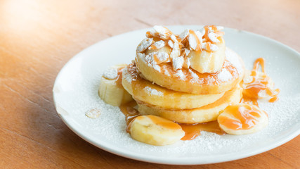 Bannana pancake toping with icing sugar,banana,caramel and almond on wooden table,lighting from behide. © shinji3802