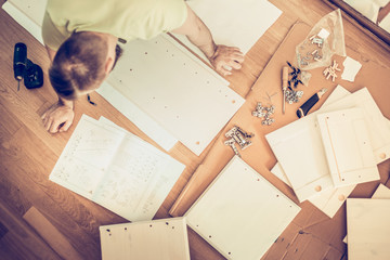 young man collect furniture and refer to the instructions laid out around the details and istrument