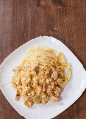 Sliced fried chicken meat in a creamy sauce with spaghetti pasta in a plate on wooden table