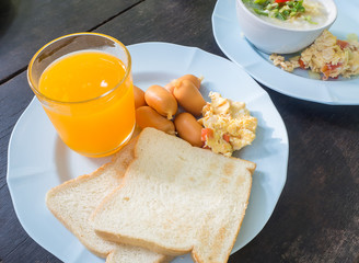 Scrambled eggs with pork sausages, bread and orange juice on woo