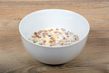Muesli with a mix of healthy fruit, nuts and seeds and milk in a dish against a wooden background.
