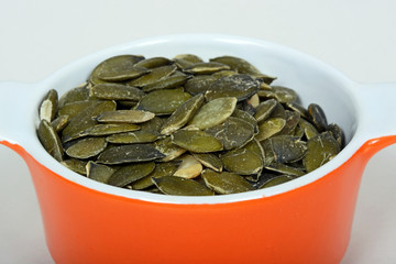 Raw pumpkin seeds in an orange ramekin dish.