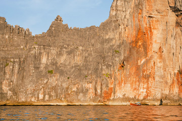 Andaman Sea cliffs and the small fishing boat driving at evening sun