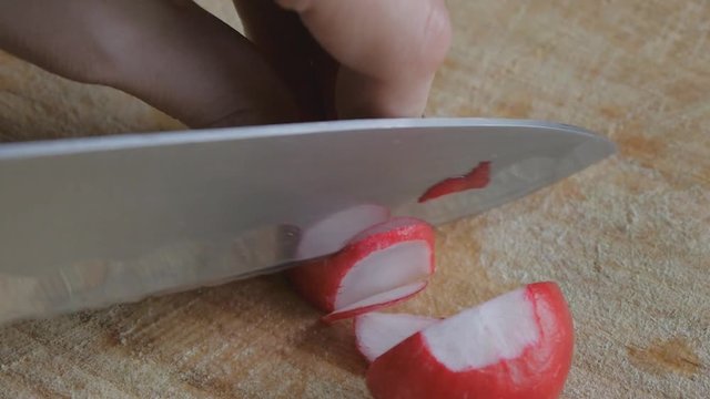 Girl's hands with red nails cut radishes into slices