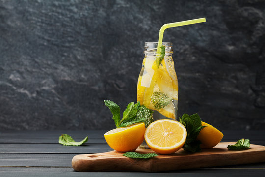 Lemonade drink of soda water, lemon and mint leaves in jar on black background