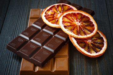 Milk, black chocolates with dry oranges on dark wooden boards