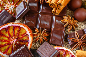 Dark and milk chocolates with dry oranges, candies, cinnamon and anise on burlap on rustic wooden table