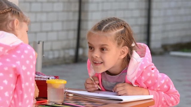 Seven-year girl drawing in an album emotionally speaks with another girl