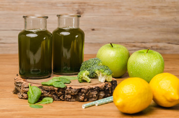 Green fresh leafy greens smoothie in glass jar, spinach leaves, apple, broccoli and lemon. Refreshing healthy drink on wooden table background