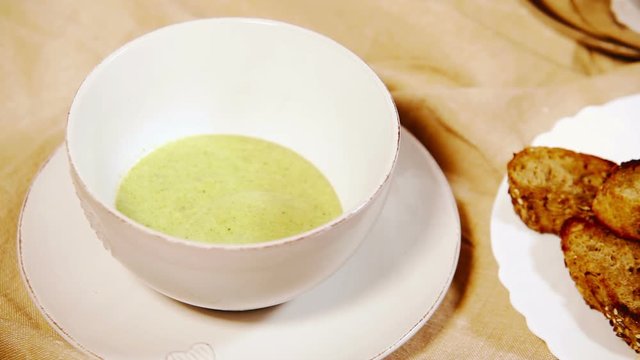 Broccoli cream soup being poured into the bowl with toasts aside