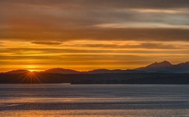Setting Sun Sparks as it Falls below Horizon and the Olympic Mountains.  Taken from Seattle, Washington