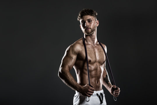 Handsome young bodybuilder training with resistance bands, on grey