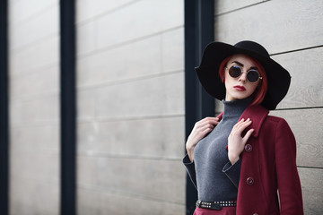 Obraz premium Closeup portrait of young beautiful fashionable woman with sunglasses. Lady posing on grey wooden background. Model wearing stylish wide-brimmed hat. Girl looking at camera. Female fashion. Copy space