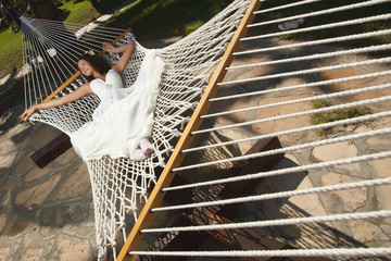 Lovely, young bride relaxing, lying on hammock under summer sun.