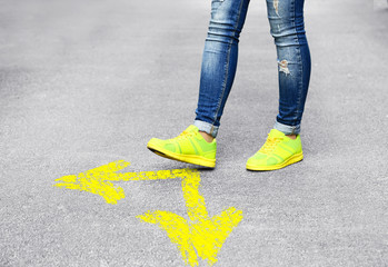 Female feet walking on road with yellow arrows