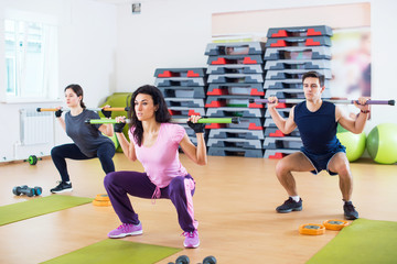 People exercising in gym doing squats working out with barbells fitness club.