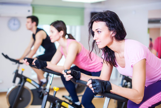 Group training people biking in the gym, exercising legs doing cardio workout cycling bikes